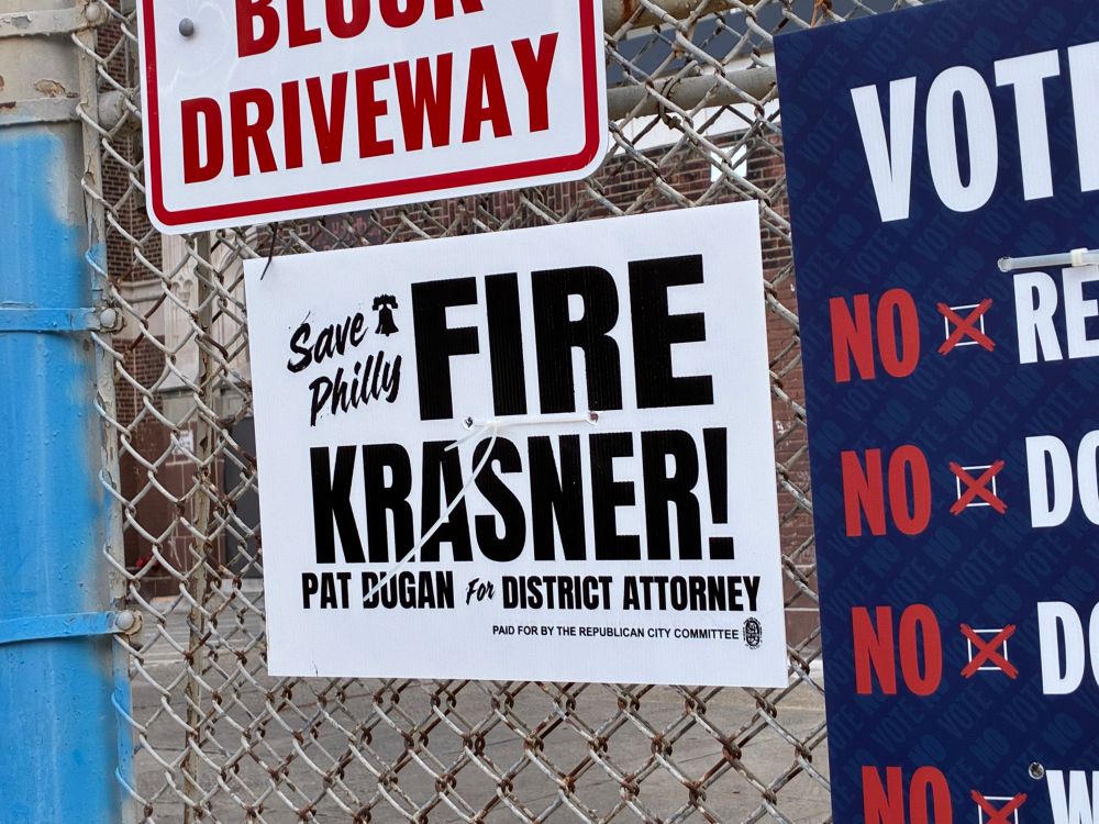 A campaign sign on a metal fence that says “save Philly Fire Krasner! Pat Dugan for district attorney.”