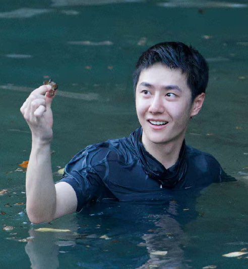 Head and shoulders shot of Wang Yibo in the water, looking excited as he holds up a crab he found