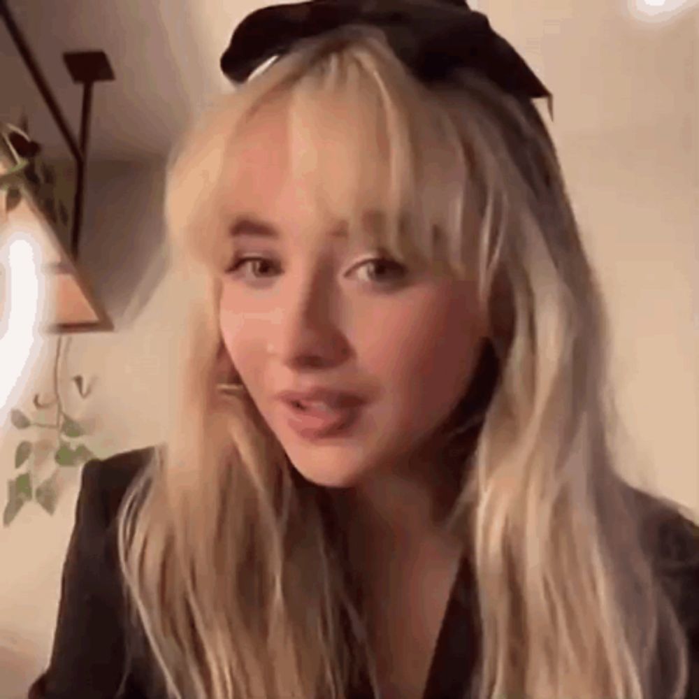 a close up of a woman with blonde hair wearing a black bow on her head .