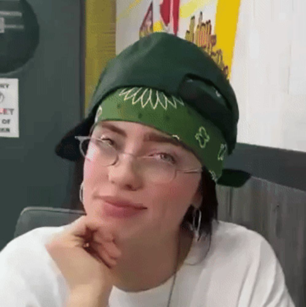 a woman wearing glasses and a green bandana looks at the camera