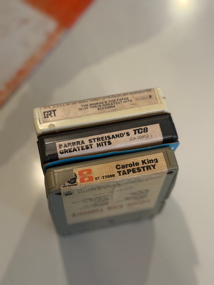 Three 8-track tapes standing upright including The Mamas and the Papas, Barbara Streisand, and Carol King. 