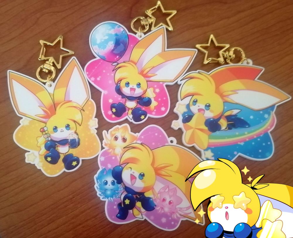 Photograph of four keychains featuring the Kinoko the kuparkuke character - a pink one, a purple one, a yellow one and a blue one - with an illustration of Kinoko himself overlayed.