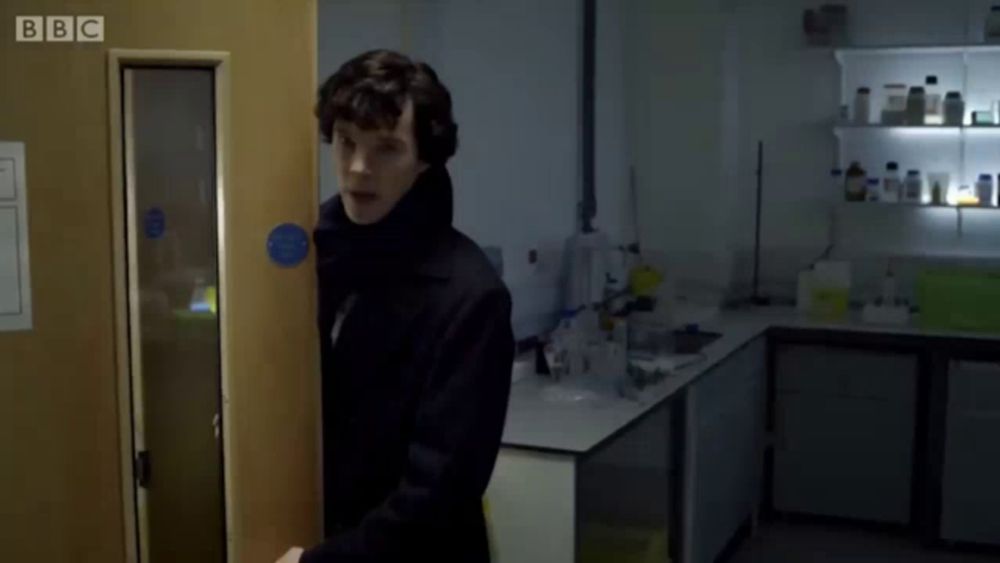 a man standing in a room with the words " the name 's sherlock holmes " on the screen