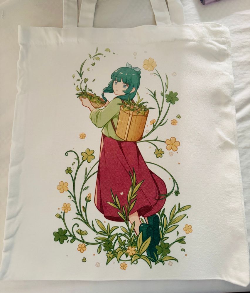 White tote bag with MaoMao from apothecary diaries in the middle surrounded by wood sorrel flowers