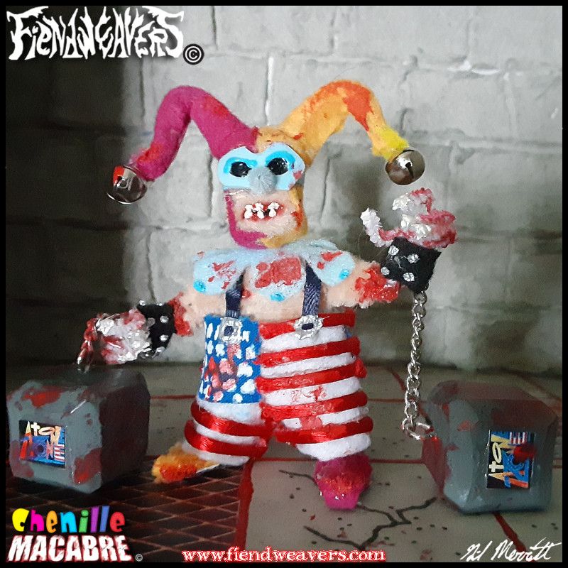 A pipe cleaner figure I built of Pugnuckle, a playable character in my tabletop splatter fighting game AMPUTHEATRE. Pugnuckle is a street clown in a magenta and gld jester's cap ending in bell. He wears a light blue mask and collar, and his oversized clown suspenders resemble the United States flag. Cained to his raw and bloody wrists are tow square bricks reading "AtoneZone". He is covered in blood. His arms and head come off for AMPUTHEATRE combat, and he stands 3" (7.62 cm) high.