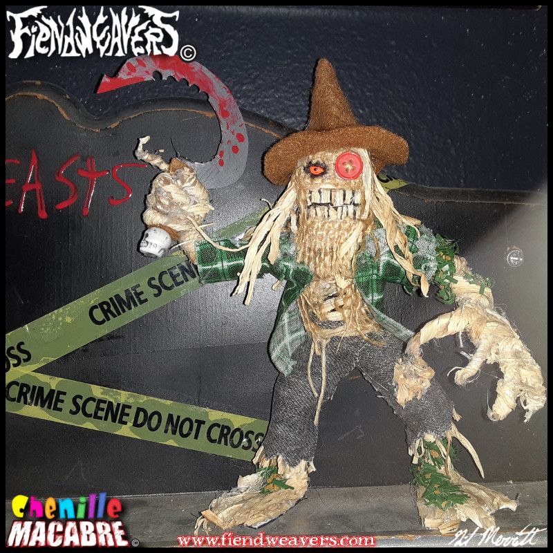 A pipe cleaner figure I built of an Evil Scarecrow. It has long straw hair, a burlap face, a straw sneer, one orange eye and one button eye. It wears a brown hat, green flannel shirt, and torn jeans. It wields a bloody serrated sickle, and stands 5