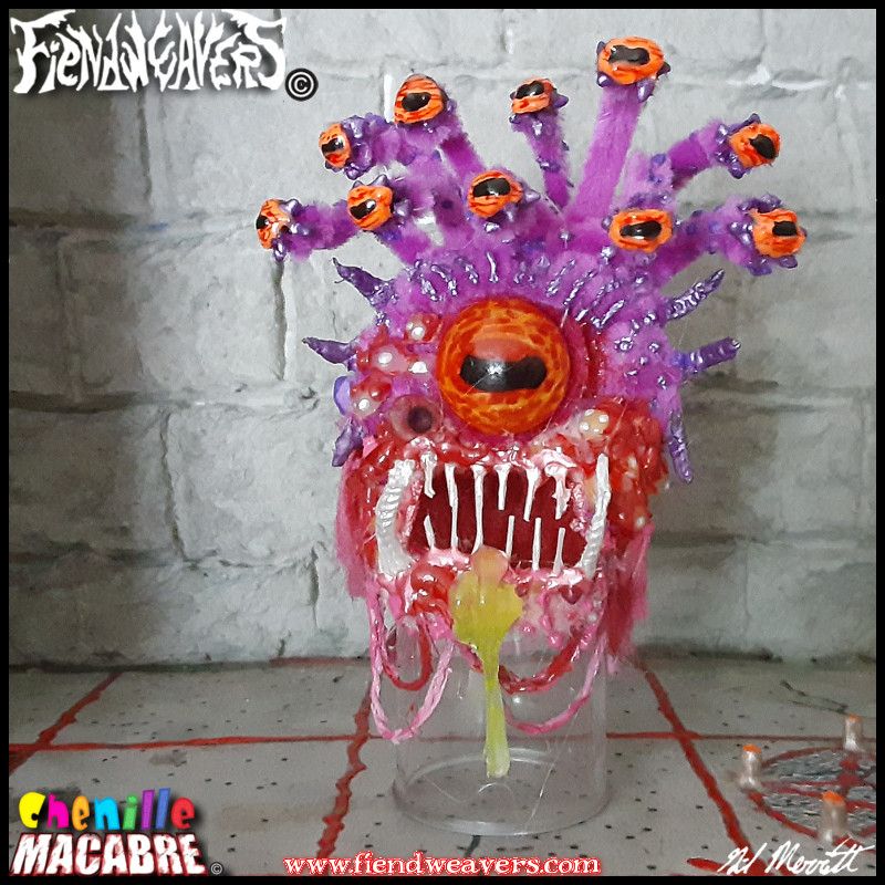 A pipe cleaner figure I built of a Beholder from the tabletop roleplaying game Dungeons & Dragons. It is a spherical floating monster with eleven eyes (ten on stalks and one large central) and a gaping maw. This specimen is a light purple with needle teeth and rotting gums and jaws. A glob of drool forms at its lip.