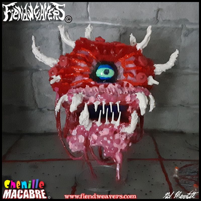 A pipe cleaner figure I built of the Cacodemon from the video game DOOM. The Cacodemon is a red and pink floating spherical monster with a single green eye, a heavily fanged mouth, and sharp horns. Flesh dribbles and hangs underneath it in strands and loops. It stands 3" (7.62 cm) high.