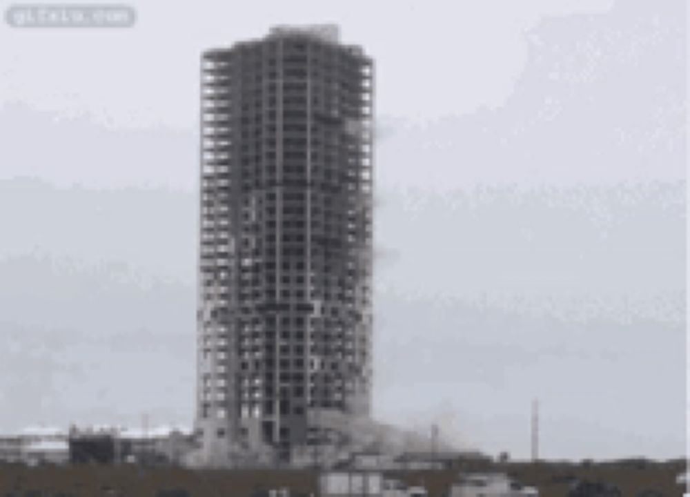 a very tall building is being demolished with smoke coming out of it .