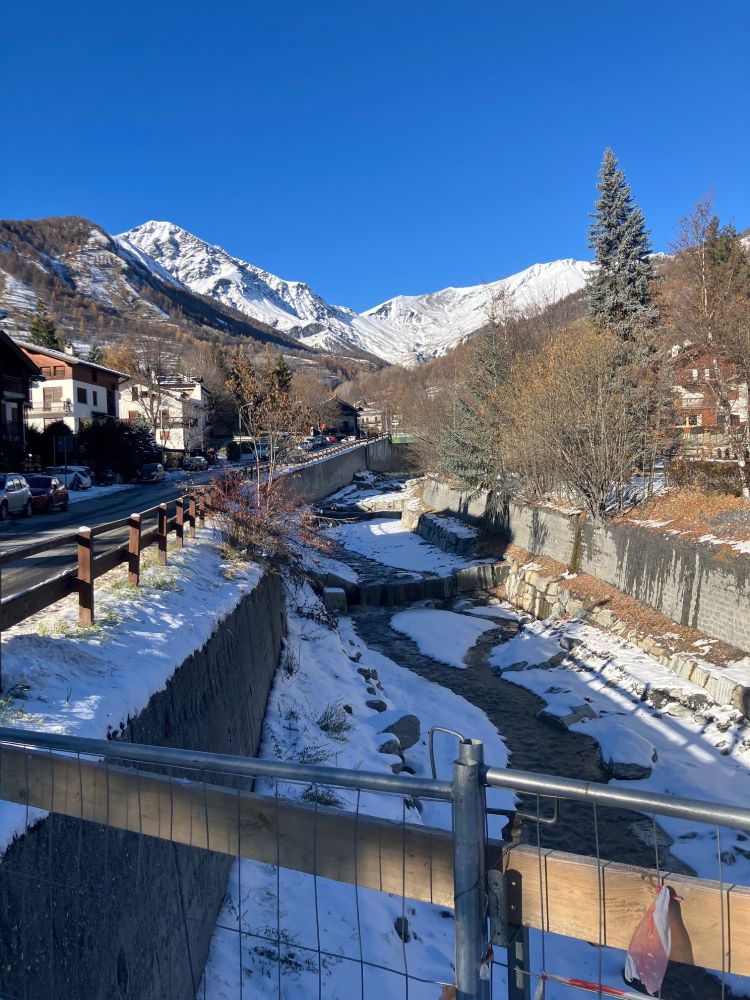 A small mountain stream channeling its way through Bardonecchio with snowcapped Alps in the background. 