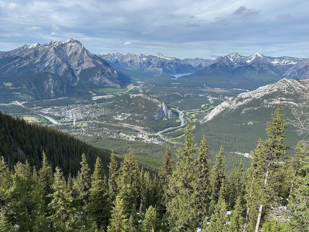 The town of Banff, Canada, surrounded by rugged, snow capped mountains. The photo is taken from the top of one of the mountains looking down towards the town.