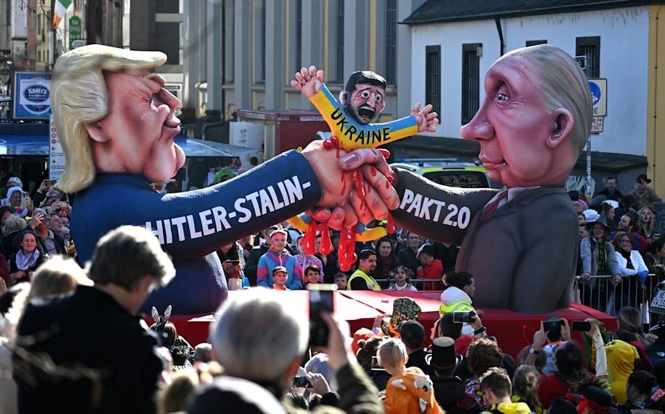 A colorful parade float depicting Trump and Putin shaking hands with Zelinsky being bloodily squeezed between their fingers