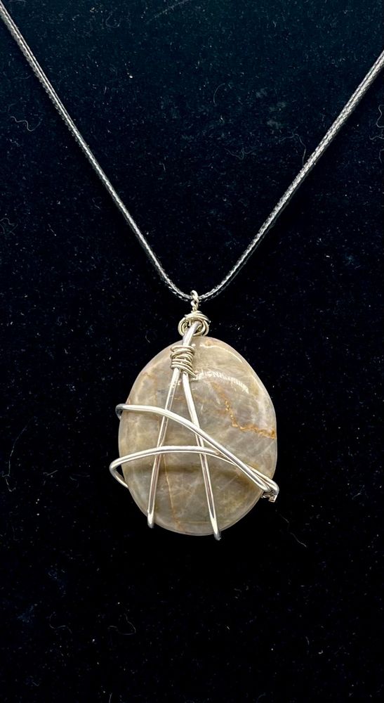 Closeup of dove gray tumbled agate stone pendant wrapped in silver wire and strung on a black leather cord. 