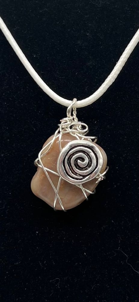 Closeup of pink tumbled stone pendant with a silver spiral bead, wrapped in silver wire and strung on a white leather cord. 