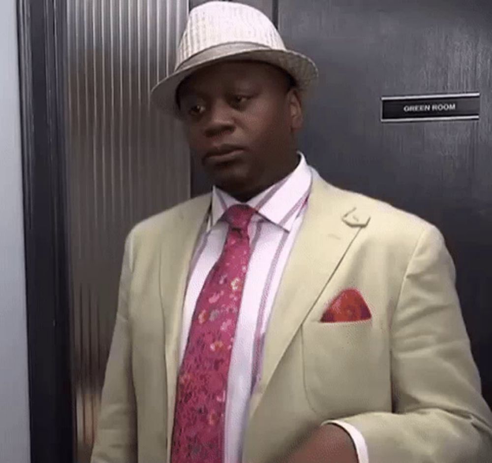 a man in a suit and hat is standing in front of a green room door .