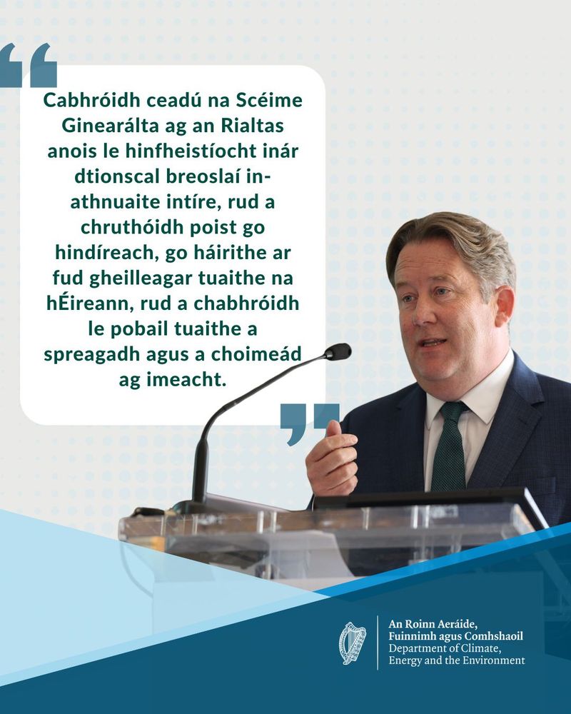 Minister O'Brien gestures while presenting text in Irish about government initiatives related to energy and public involvement at a podium.