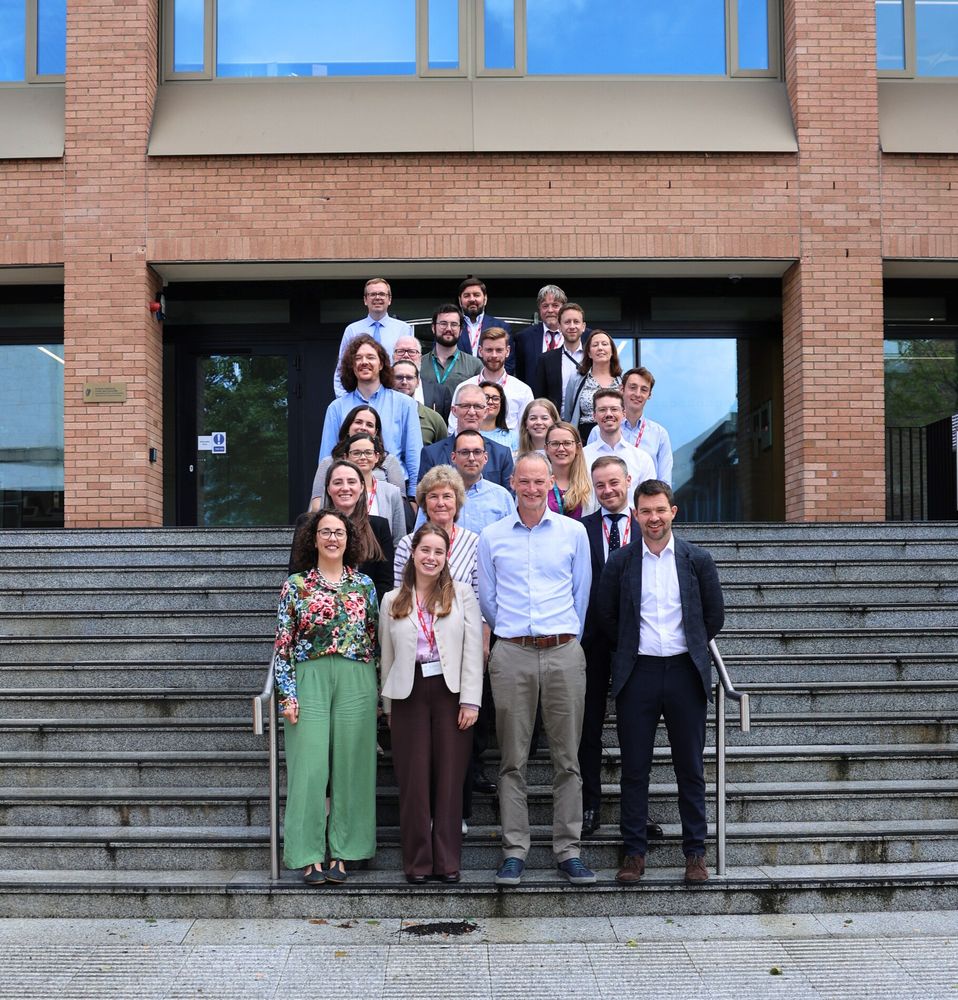 Group photo of a diverse assembly of professionals posing on outdoor steps, in front of a modern brick building with large windows.