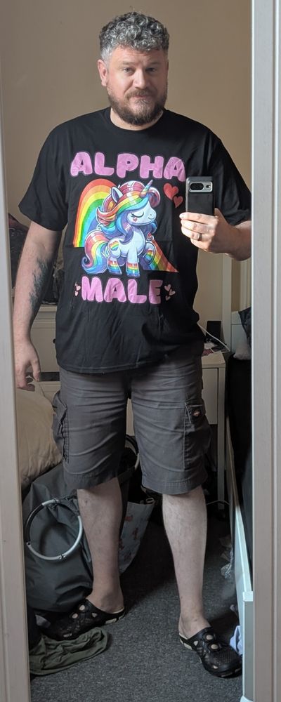 A picture of a man wearing a funny T-shirt.  The T-shirt has a picture of a unicorn and a rainbow, juxtaposed with the slogan alpha male.