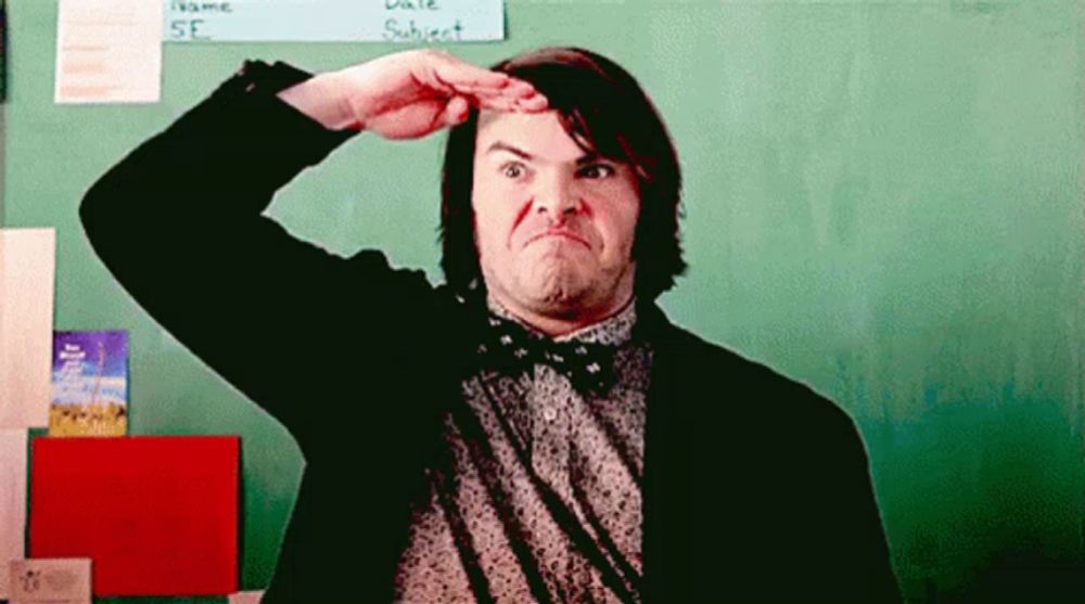 a man in a suit and bow tie is making a funny face in front of a chalkboard .