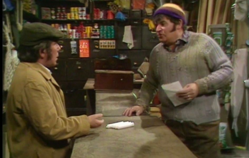 The Two Ronnies in the "Four Candles" sketch. Corbett the shopkeeper of the hardware shop gesturing to the four candles on the counter as Barker the customer tells him he's wrong. 