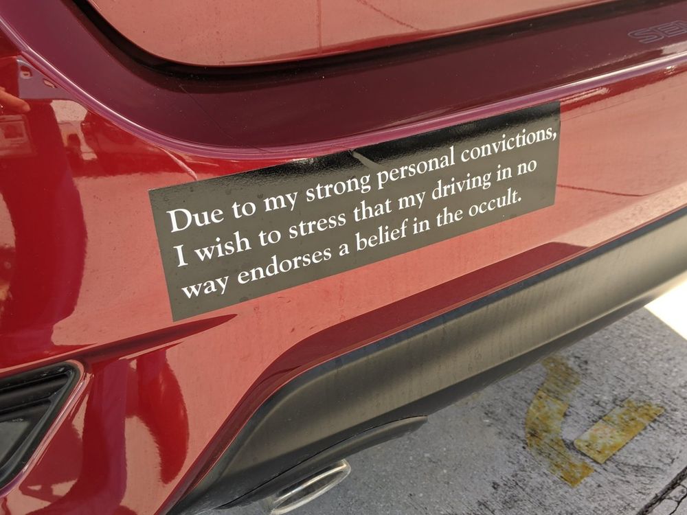 bumper sticker on the back of a red car that says "due to my strong personal convictions, I wish to stress that my driving in no way endorses a belief in the occult"