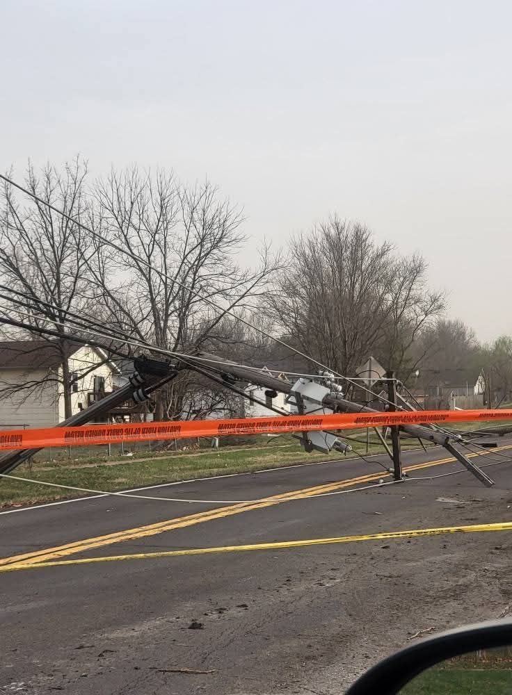 Picture of a downed powerline laying across a road with police tape blocking off access to the road. 
