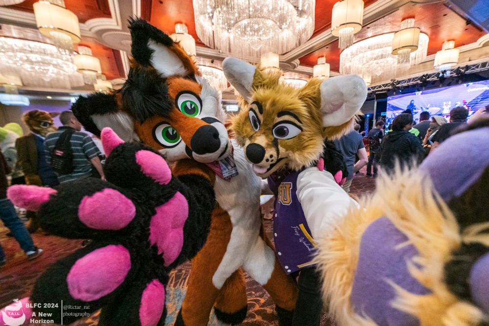 2 natural colored brown fursuiters have their paws outstretched towards the camera a in a large ballroom 