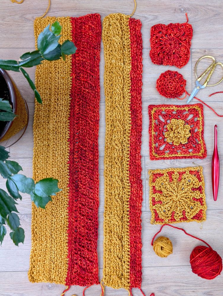 Six pieces of a crochet blanket displayed on a wood background. The crocheter is using red and gold yarn. The photo also features a pair of gold scissors, a red crochet hook, and a plant peeking in on the left side of the frame. 
