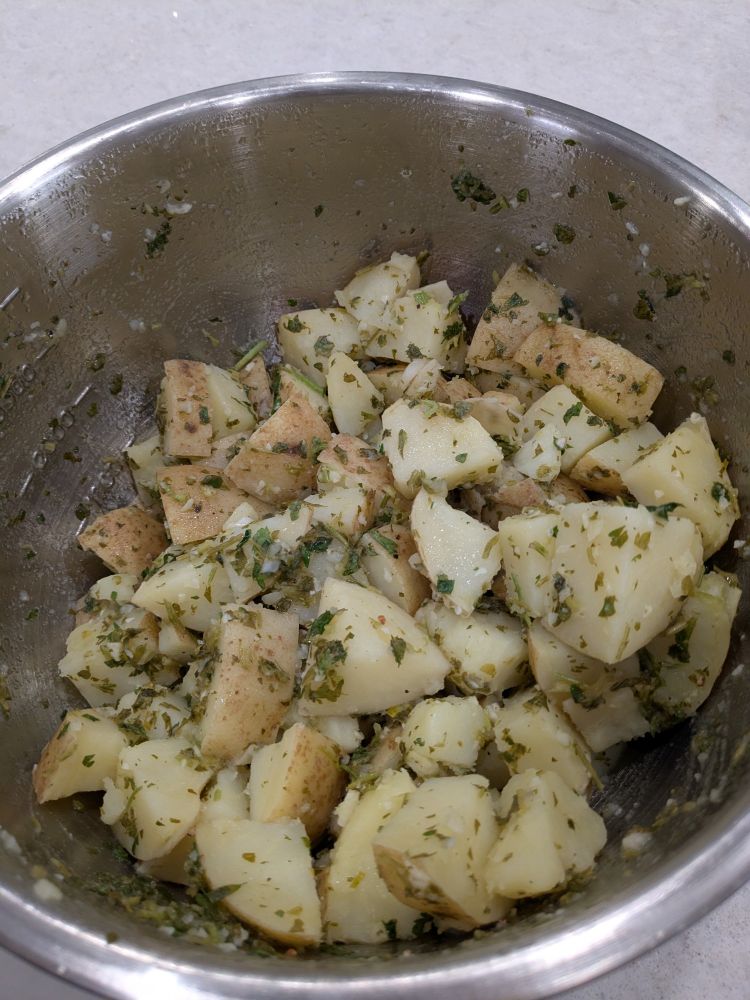 Potato salad in a large metal bowl. Potatoes aren't peeled and parsley is visible throughout 