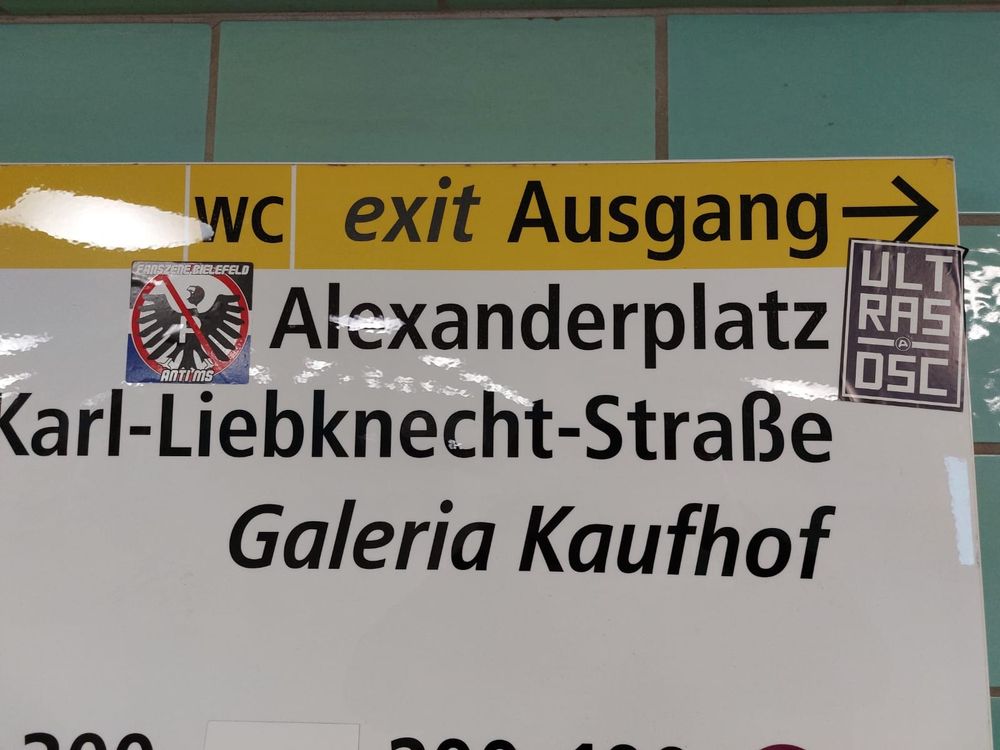 Arminia Sticker auf dem Hinweisschild zum Ausgang zum Alexanderplatz. Einer zeigt die Abneigung zu Preußen Münster und der andere hat die Aufschrift Ultras DSC