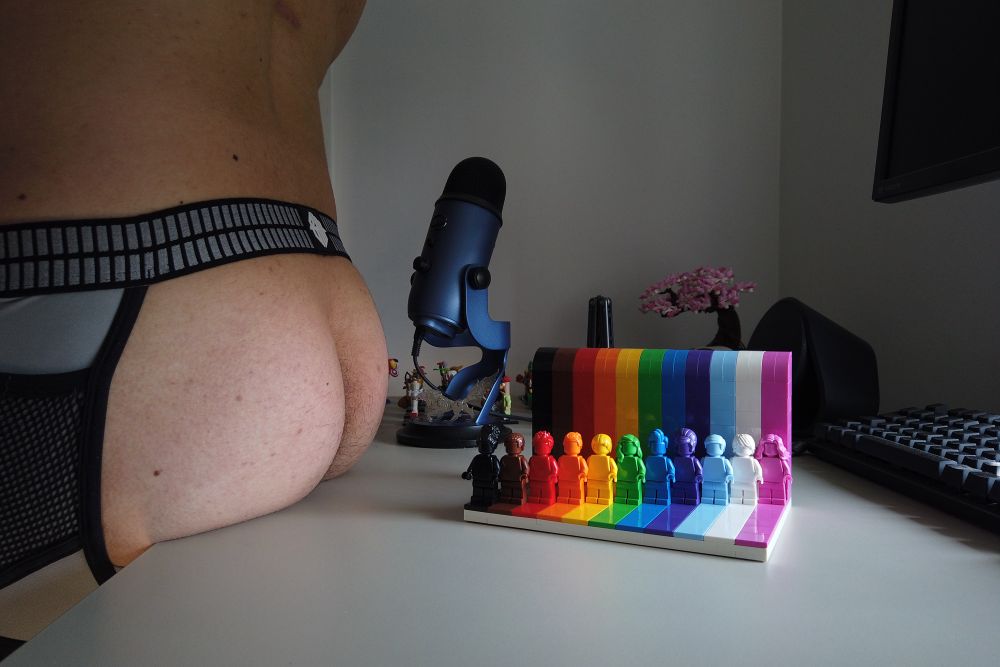 Pup Danny's ass in a jockstrap next to a LEGO everyone is awesome set, his ass is gently resting on the table.