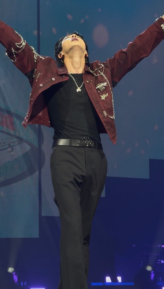 Seokjins itty bitty waist on prominent display. He’s singing into a pink mic with his left hand, his right arm is stretched in a V showcasing his world wide handsome shoulders. The red jacket is lifting up exposing his waist and hips ✨✨sluttily ✨✨. He’s wearing a dark red jacket with chains, his black pants shirt and belt that says Jin. The background is blue with pink confetti for spring day