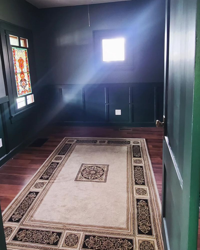 A room painted green with a stained glass window and a tan rug