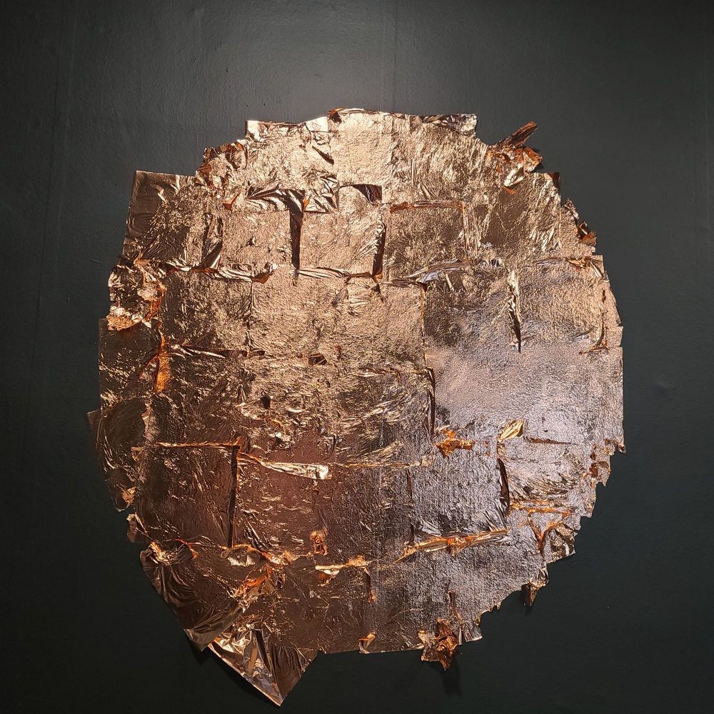 A rough circle of still somewhat loose copper leaf on a painted wall