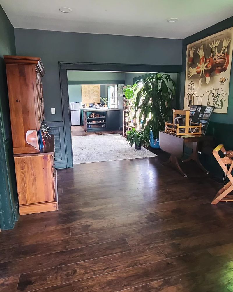 A long room with green walls, wood floors, and plenty of plants. 