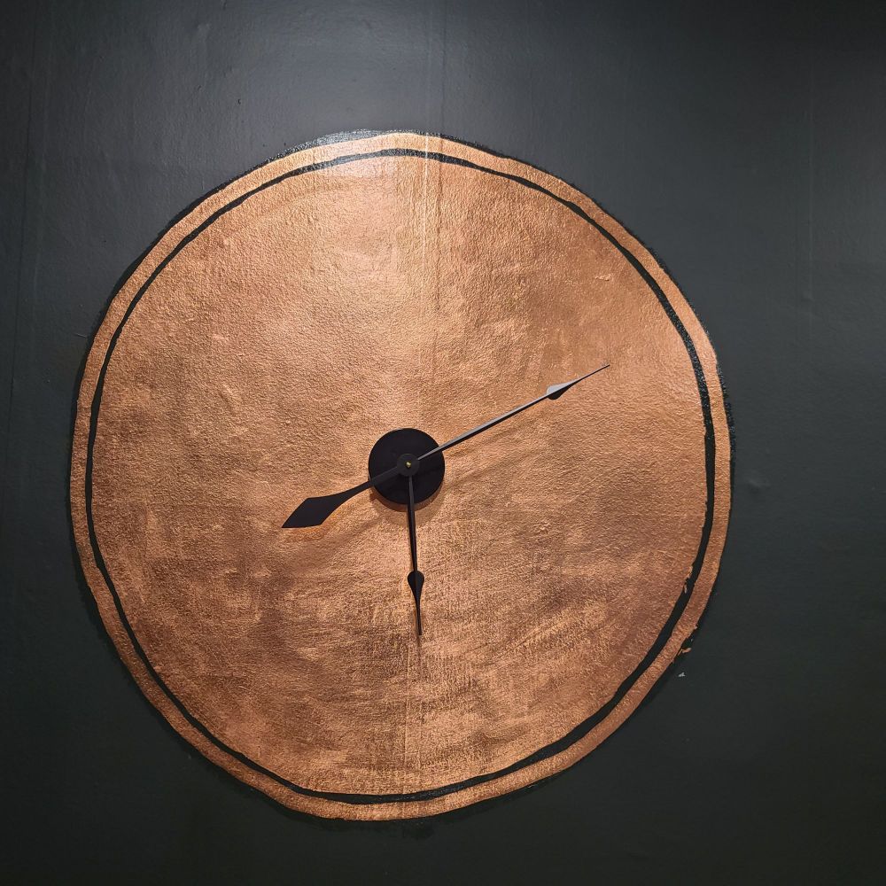 A circle of copper leaf on a dark painted wall with a clock mechanism set in the center
