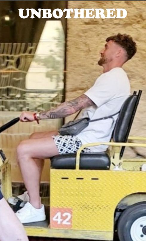 Dan Scarr is seated on a yellow luggage cart, holding the wheel with one hand and looking straight ahead with a chill expression. Scarr appears completely at ease, like driving through luxury hotels on a luggage cart is part of his daily routine.