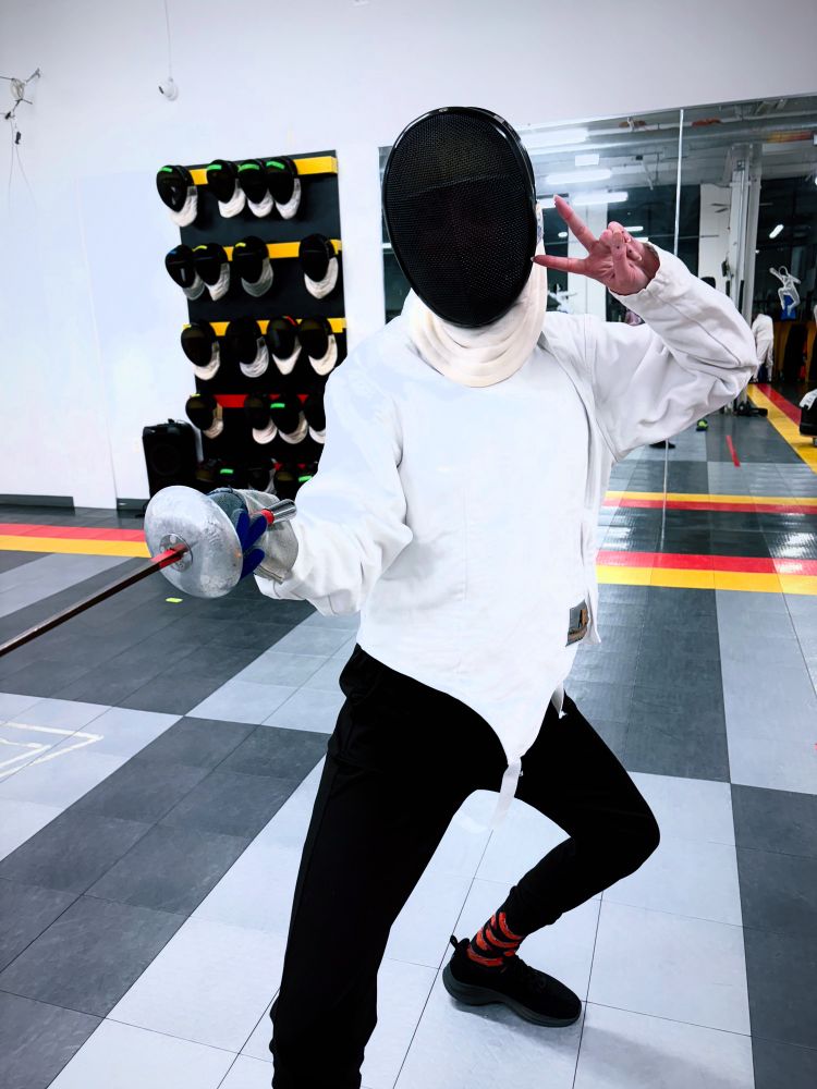me in upper fencing gear, en guard, holding up peace sign