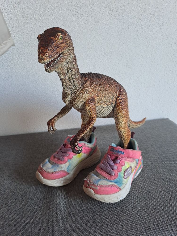 Ein Spielzeug Dinosaurier "Raptor" trägt Kinderschuhe.