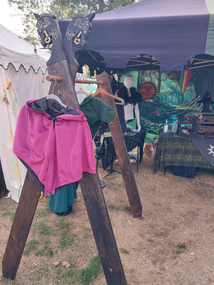 A wooden clothing rack in front of a medieval tent setup with two remaining pieces on it with empty hangers