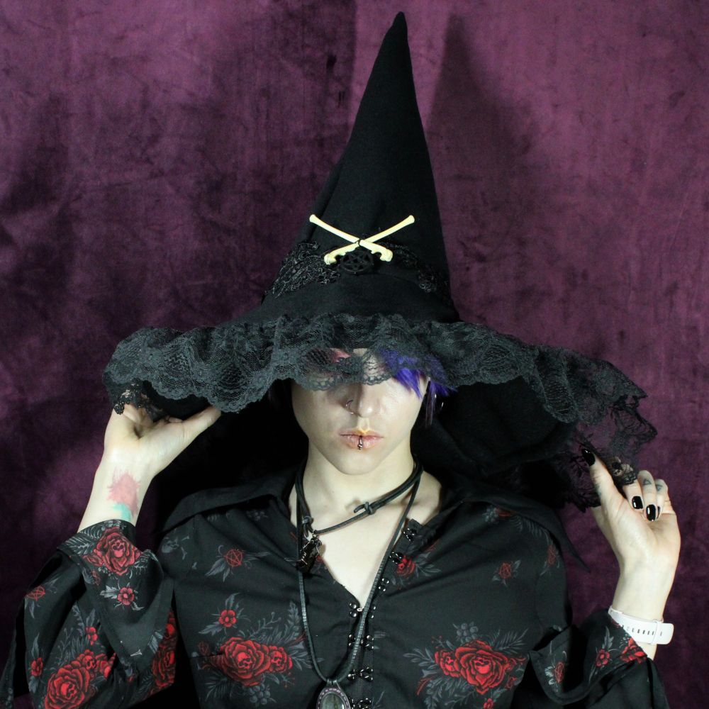 Alt model wearing an oversized black gothic style pointed hat with bones and lace