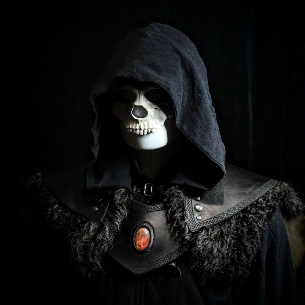 A mannequin with a black hood obscuring it's masked face wearing leather armor with a labradorite crystal and sheep skin