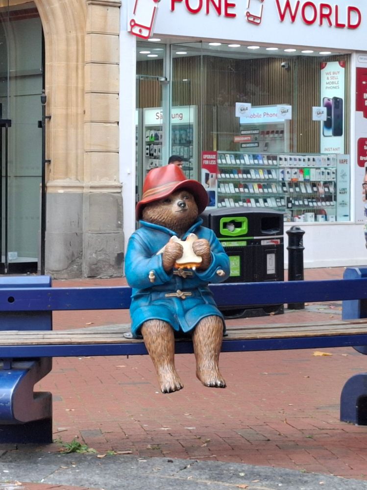 Paddington Bear sitting on a bench in the center of Reading.
Paddington Bär auf einer Bank sitzend im Zentrum von Reading. 