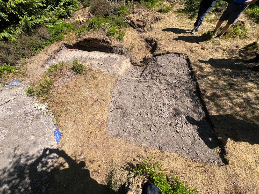 Small slit trench half of which has been excavated by archaeologists. Next to the trench is a mound of earth that was the upcast of the trench used as a firing platform 