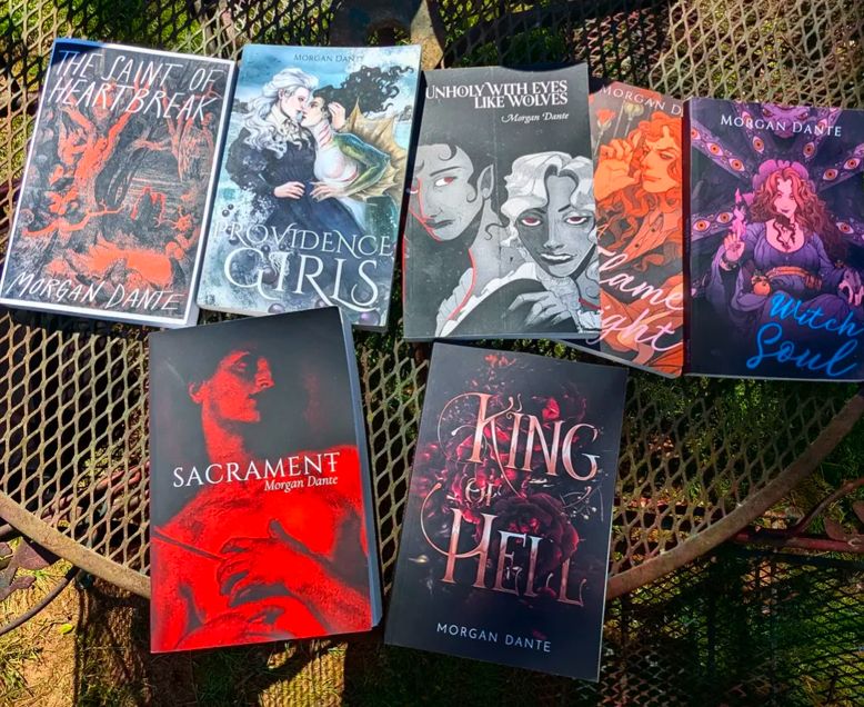 Morgan Dante books on a table outside. Top row: The Saint of Heartbreak, Providence Girls, Unholy With Eyes Like Wolves, A Flame in the Night, and Witch Soul. Bottom row: Sacrament and King of Hell.