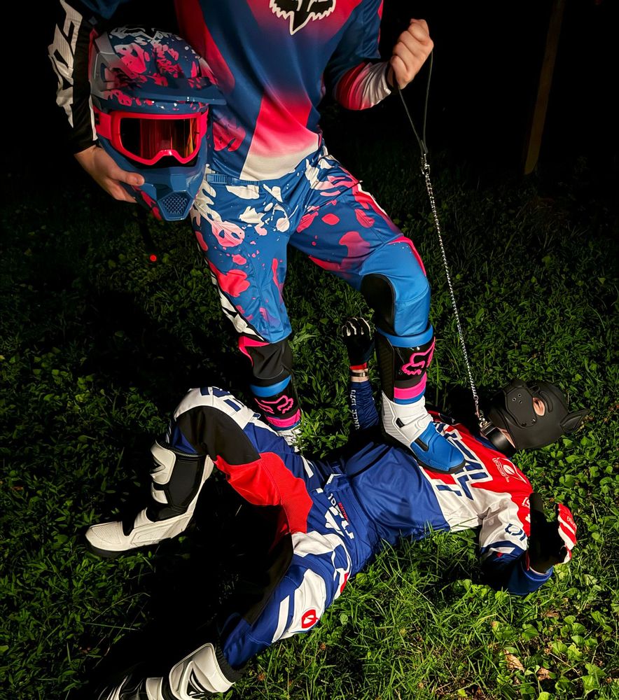 max grabbing me by the leash and stomping me on the chest. we're both wearing red white and blue motocross gear. I'm in a black pup hood