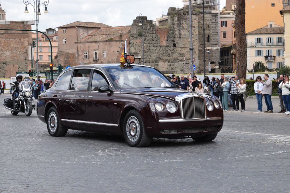 A car going down a road with tourists and bystanders watching.