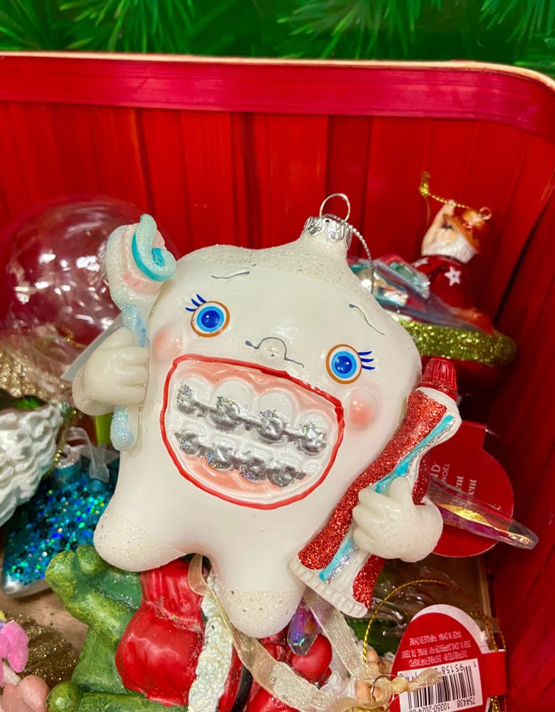 Picture of a glass tree ornament. Design is a humanoid human tooth with an enormous smile, braces, and holding a toothbrush. 
