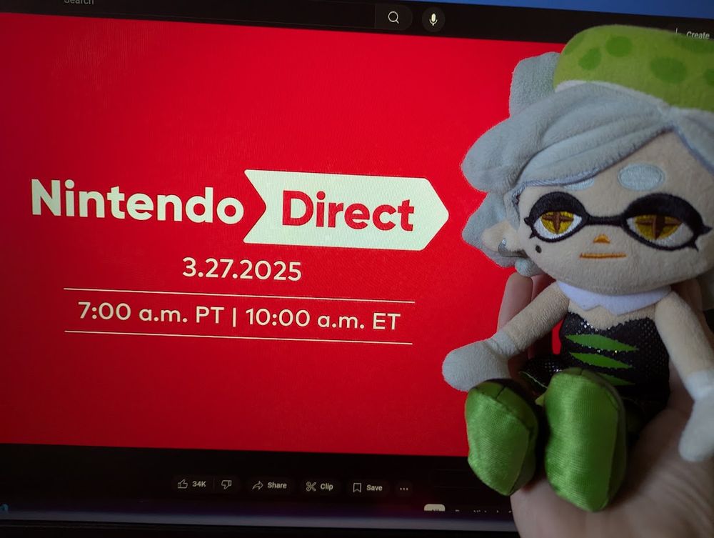 Marie Plush is being held in front of a computer screen showing the March 2025 Nintendo Direct livestream waiting screen on YouTube.
