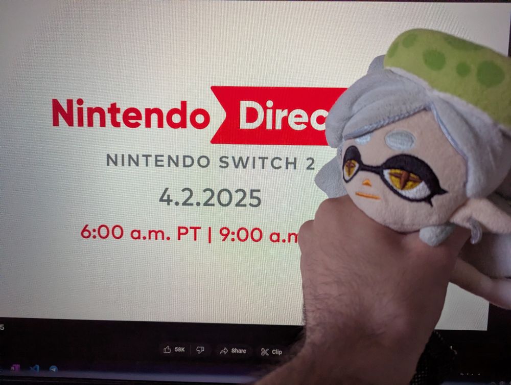 Marie Plush is being grabbed in a chokehold in front of a computer screen showing the Switch 2 Direct livestream waiting screen on YouTube.
